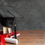 a graduation cap on top of books and a diploma scroll tied with red ribbon