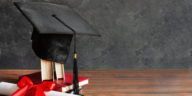 a graduation cap on top of books and a diploma scroll tied with red ribbon