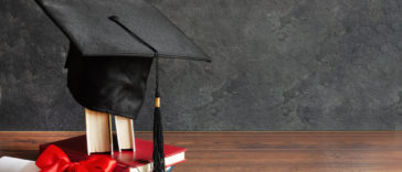 a graduation cap on top of books and a diploma scroll tied with red ribbon