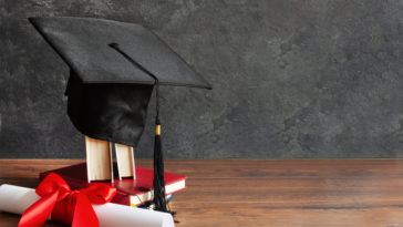 a graduation cap on top of books and a diploma scroll tied with red ribbon