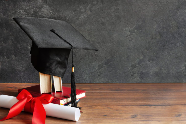 a graduation cap on top of books and a diploma scroll tied with red ribbon