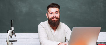 man sitting at a table typing on a laptop in front of a chalkboard