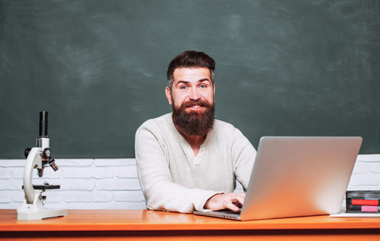 man sitting at a table typing on a laptop in front of a chalkboard