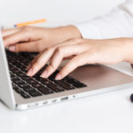 woman in white shirt typing on a laptop