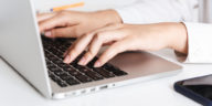 woman in white shirt typing on a laptop