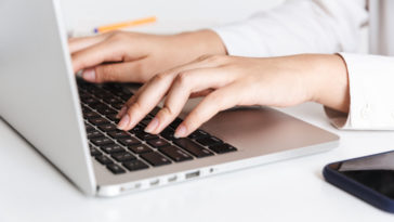 woman in white shirt typing on a laptop