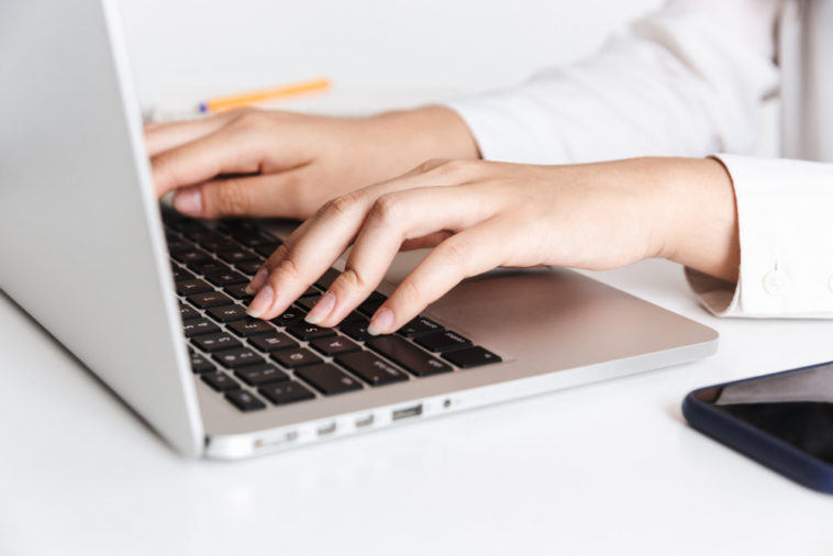 woman in white shirt typing on a laptop