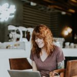 smiling woman sitting with laptop in coffee shop