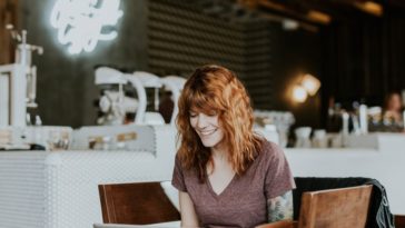 smiling woman sitting with laptop in coffee shop
