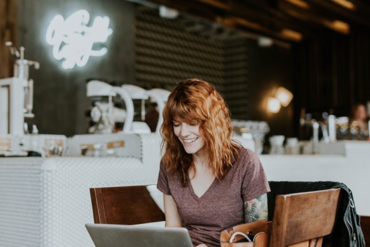 smiling woman sitting with laptop in coffee shop