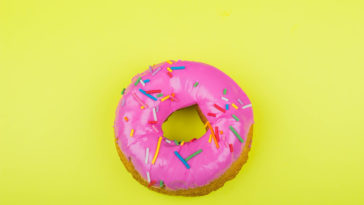 donut with pink glaze with a yellow background