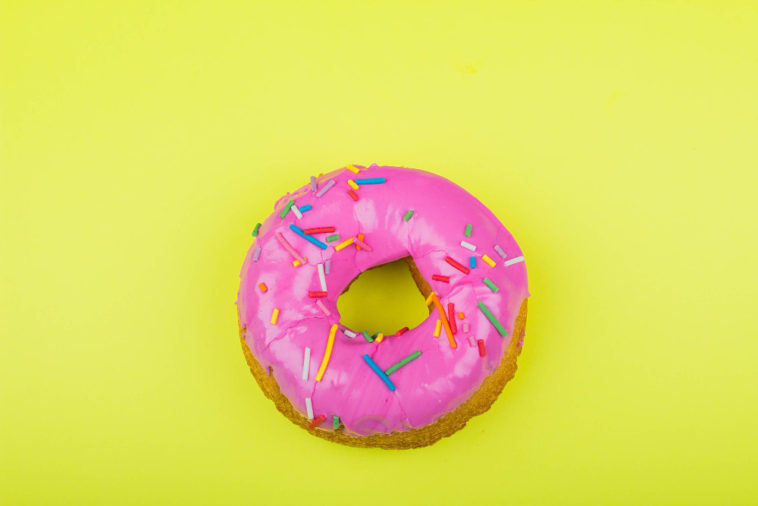 donut with pink glaze with a yellow background