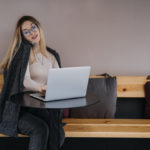 woman sitting at a table talking on a phone and typing on a laptop