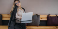 woman sitting at a table talking on a phone and typing on a laptop