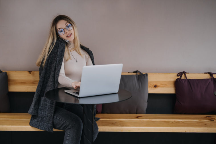 woman sitting at a table talking on a phone and typing on a laptop