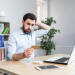 frustrated man in front of a laptop looking at a credit card