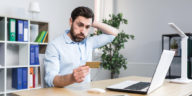 frustrated man in front of a laptop looking at a credit card