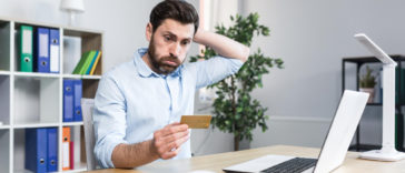 frustrated man in front of a laptop looking at a credit card