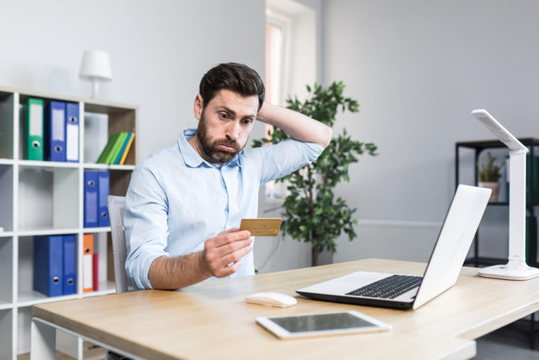 frustrated man in front of a laptop looking at a credit card