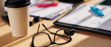 office table with glasses, papers with marker and coffee cupr