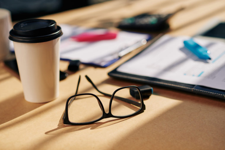 office table with glasses, papers with marker and coffee cupr