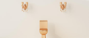 gold toilet bowl in front of a cream color wall