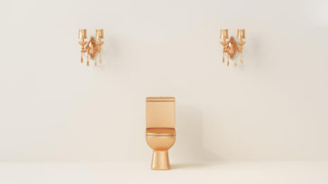 gold toilet bowl in front of a cream color wall