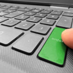 finger pointing at a green enter button of a laptop