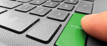 finger pointing at a green enter button of a laptop