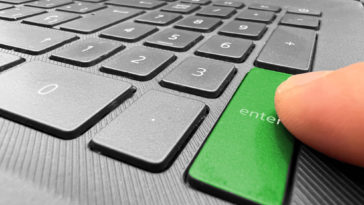 finger pointing at a green enter button of a laptop