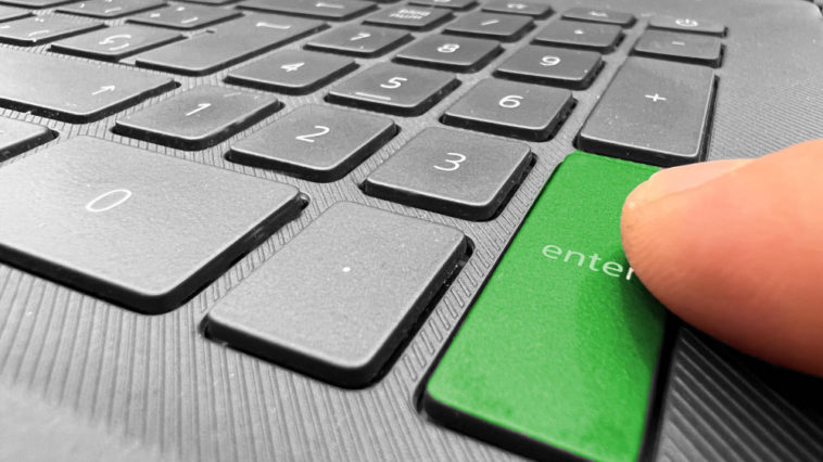 finger pointing at a green enter button of a laptop