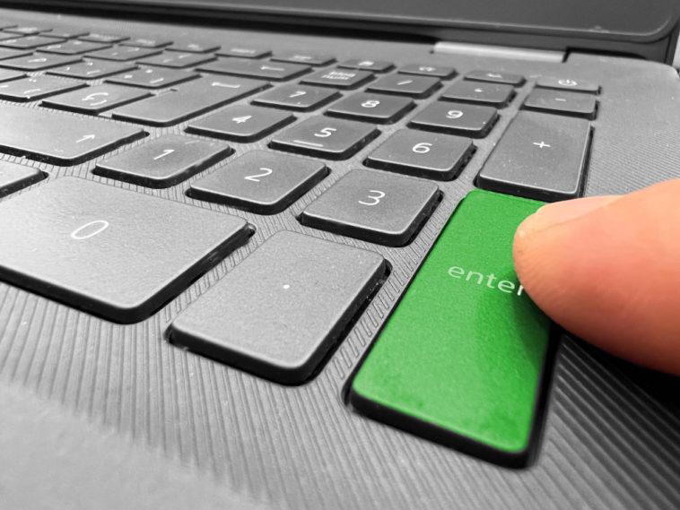 finger pointing at a green enter button of a laptop