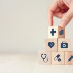 a hand stacking wood cubes with medical icons on them