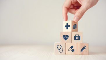 a hand stacking wood cubes with medical icons on them