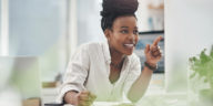 woman looking at a screen smiling and taking notes