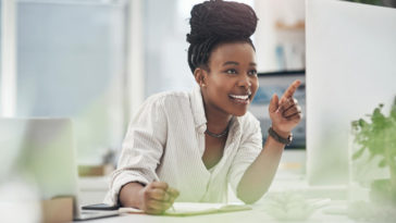 woman looking at a screen smiling and taking notes