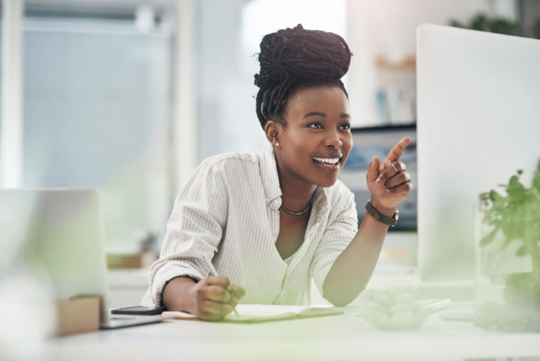 woman looking at a screen smiling and taking notes