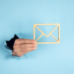 hand coming through a blue wall holding a wooden envelope sign