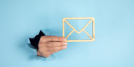 hand coming through a blue wall holding a wooden envelope sign