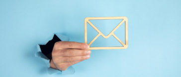 hand coming through a blue wall holding a wooden envelope sign