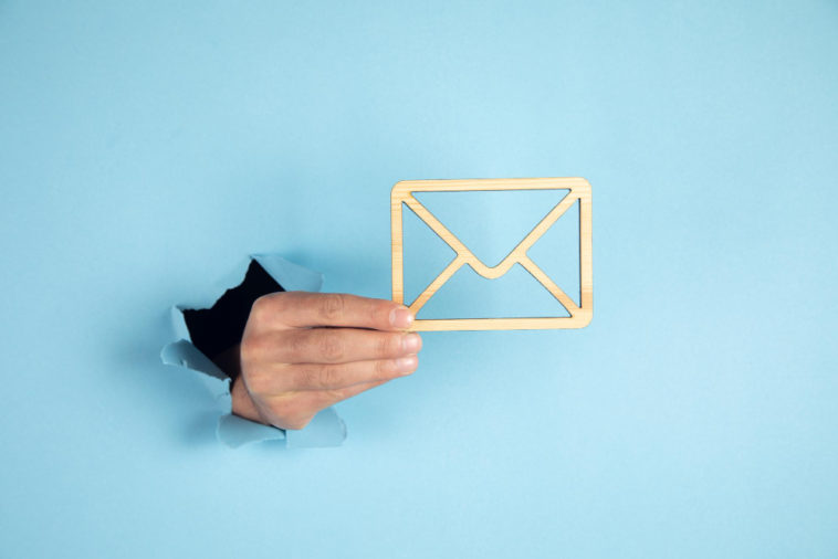 hand coming through a blue wall holding a wooden envelope sign