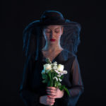 mournful woman dressed in black holding white roses