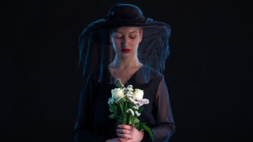 mournful woman dressed in black holding white roses