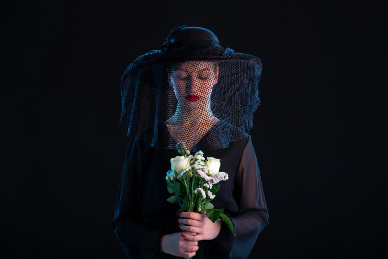 mournful woman dressed in black holding white roses
