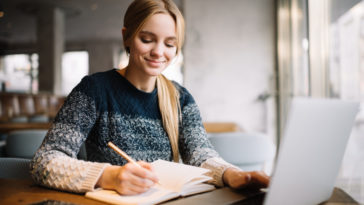 woman writing in a notebook while using a laptop