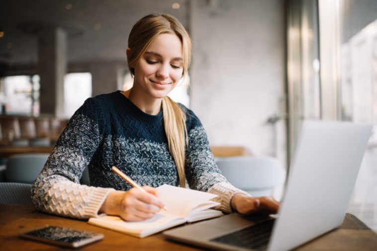 woman writing in a notebook while using a laptop