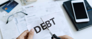 hands holding scissors cutting paper with word debt written