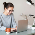 woman sitting at a table typing on a laptop