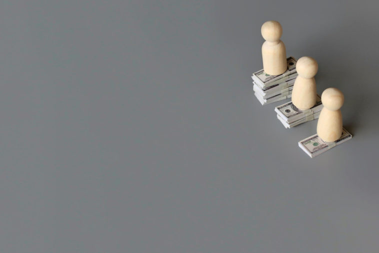 wooden figures on three different stacks of money