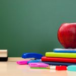 school supplies on a desk in front of a chalkboard